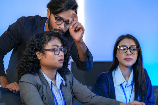 A diverse team of three developers brainstorming a solution. A male lead gestures at the screen while female colleagues analyze the complex problem in a modern tech office. - Powered by Adobe