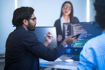 A happy and diverse tech team celebrates a successful project outcome. Smiling colleagues, led by their manager, look at the results on a computer in a modern office.