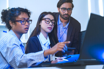 A happy and diverse tech team celebrates a successful project outcome. Smiling colleagues, led by their manager, look at the results on a computer in a modern office.
