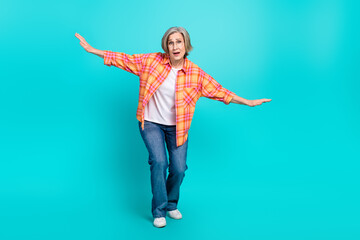 Charming elderly woman in casual plaid shirt posing playfully with a cheerful smile on turquoise background