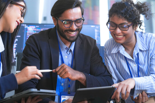A team of software engineers celebrates a successful code deployment. They review the final user interface (UI) and user experience (UX) on a tablet after a collaborative debugging session.