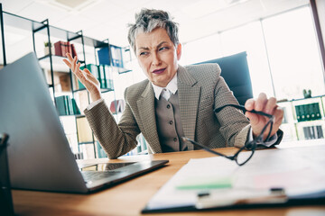 Confident senior businesswoman analyzes on computer at office while wearing formal attire and expressing critical thinking