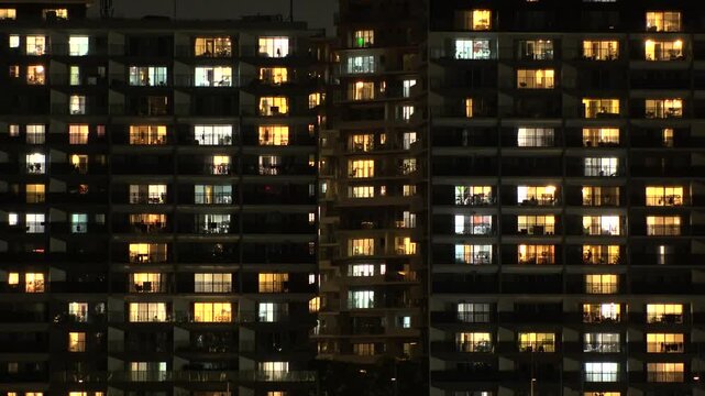 Time lapse shot of illuminated modern high rise residential apartment building with glowing windows in dense urban cityscape at night. Lifestyle and real estate concept. Shot in Tokyo, Japan.