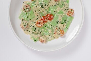 Green vegan ravioli with creamy sauce and cherry tomatoes, top view