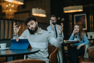 Dynamic cafe with a focus on a man engaged in multitasking on his phone and tablet, surrounded by other customers. The setting emphasizes activity, technology, and modern lifestyle in public spaces.