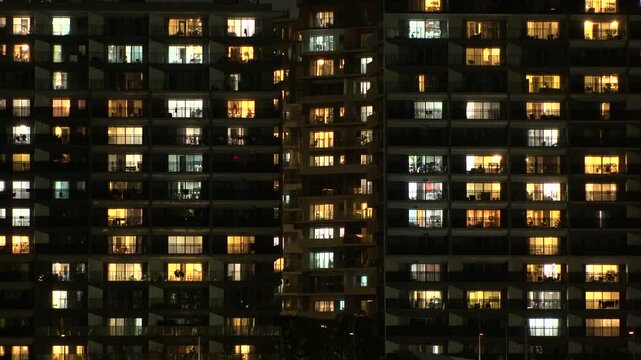 Close up shot of illuminated modern high rise residential apartment building with glowing windows in dense urban cityscape at night. Lifestyle and real estate concept video. Shot in Tokyo, Japan.