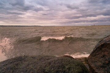 Waves crash against rocky shore under cloudy sky at coastal location during late afternoon
