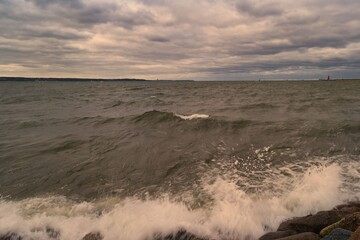 Cloudy sky over turbulent waters with rocky shore viewed from coastline at sunset