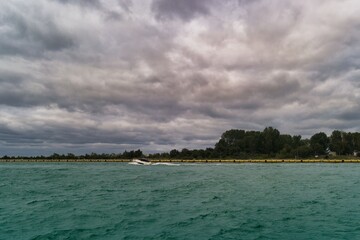 Cloudy coastal view with gentle waves and lush greenery along the shore at dusk