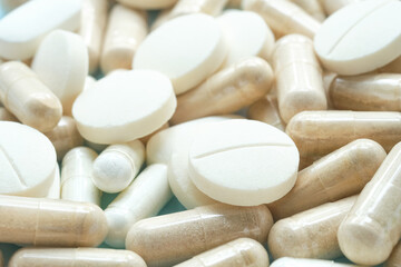 Macro shot of white tablets and supplement capsules scattered together. Blur and selective focus