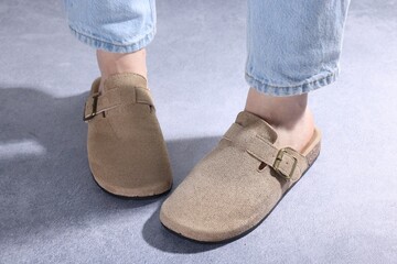 Woman in stylish beige slippers on grey textured floor, closeup