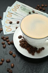 Cup of aromatic coffee, dollar banknotes and roasted beans on dark textured table, closeup