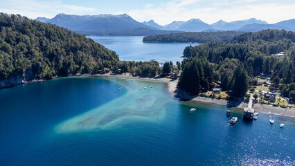 An aerial view of a stunning bay with clear blue-green water and a secluded beach near Villa La Angostura, Argentina. A beautiful Patagonian travel destination