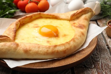 Tasty khachapuri with cheese, egg and other products on wooden table, closeup