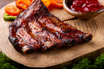 BBQ pork ribs from pork tenderloin with vegetables, cranberry sauce on board close up