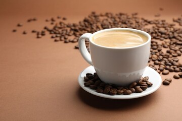 Cup of hot coffee and beans on brown background, closeup. Space for text