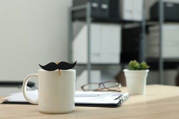 Happy Father's Day. Cup with paper moustache and clipboard on wooden table, closeup