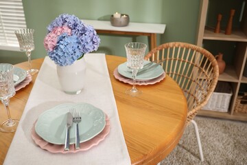 Stylish setting with plates and vase of flowers on wooden table in dining room. Interior design