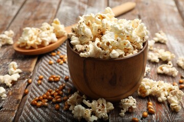Tasty popcorn and corn kernels on wooden table, closeup