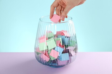 Woman taking pink paper piece from glass jar on color background, closeup