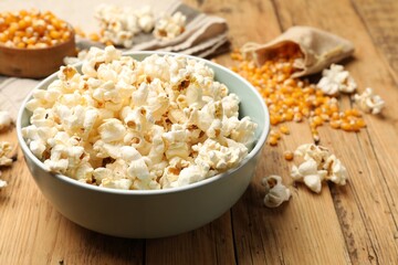 Tasty popcorn and corn kernels on wooden table, closeup