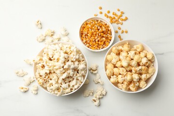 Tasty popcorn and corn kernels on white table, flat lay