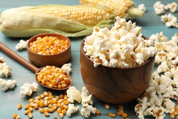 Tasty popcorn and corn kernels on blue wooden table, closeup