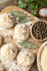 Fototapeta premium Uncooked khinkalis (dumplings) with peppercorns, flour, parsley and bay leaves on wooden table, flat lay