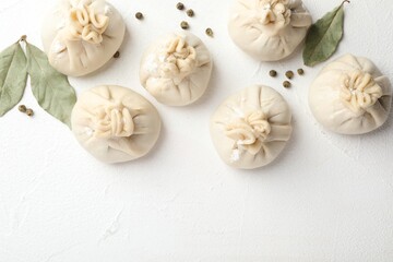 Fototapeta premium Uncooked khinkalis (dumplings) with peppercorns and bay leaves on white table, flat lay. Space for text