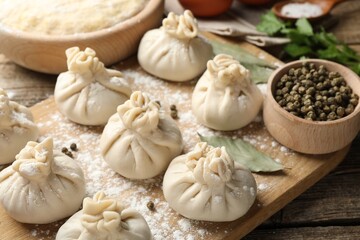 Uncooked khinkalis (dumplings) with peppercorns, flour and bay leaves on wooden table, closeup