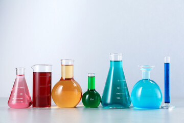 Different laboratory glassware with color liquids on light background