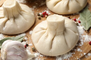 Uncooked khinkalis (dumplings) with peppercorns, flour and bay leaves on wooden table, closeup
