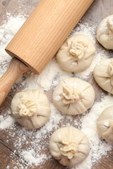 Uncooked khinkalis (dumplings) with rolling pin and flour on wooden table, flat lay