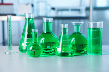 Different laboratory glassware with green liquid on light table indoors