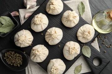 Uncooked khinkalis (dumplings) with peppercorns, garlic and bay leaves on black table, flat lay