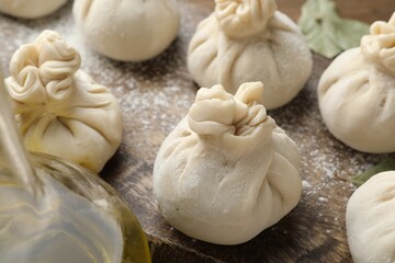 Uncooked khinkalis (dumplings) with flour and bay leaves on wooden table, closeup