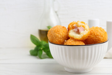Delicious fried croquette balls in bowl on white wooden table, closeup. Space for text