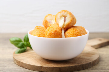 Delicious fried croquettes in bowl and basil on wooden table, closeup