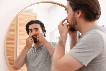 Young man with acne problem near mirror at home