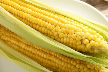 Tasty boiled corncobs with leaves on table, closeup
