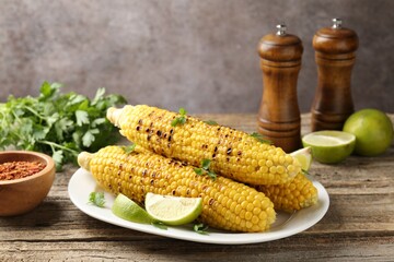 Tasty grilled corncobs with parsley and lime slices on wooden table