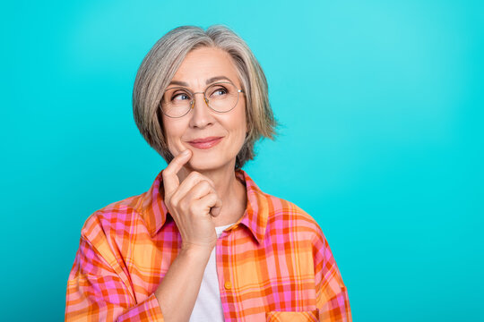 Portrait of a smiling mature woman with short gray hair against a turquoise background wearing a casual checkered shirt