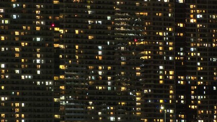 Time lapse shot of illuminated modern high rise residential apartment building with glowing windows in dense urban cityscape at night. Lifestyle and real estate concept.