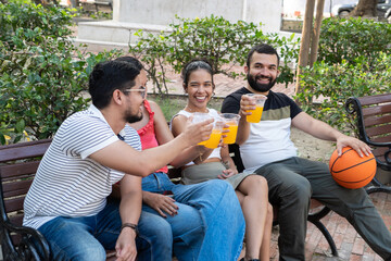 Group of friends toasting with orange juice after playing basketball in park
