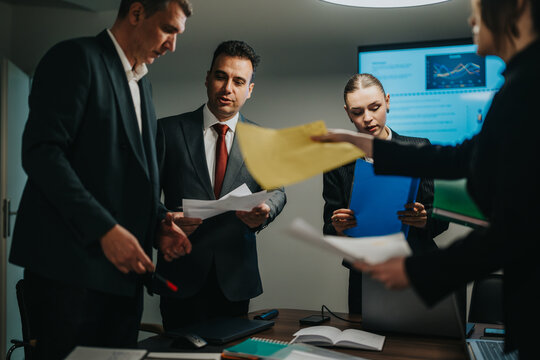 A business team engages in reviewing documents and analyzing graphs in an office meeting room with modern technology. - Powered by Adobe