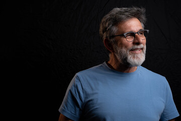 Mature man smiling and looking towards light against black background, positive chiaroscuro portrait, hope concept