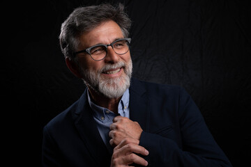 Mature bearded businessman in confident portrait with chiaroscuro lighting on dark studio background, low key style
