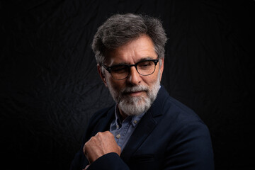 Bearded mature businessman in serious low key portrait isolated on dark studio background with chiaroscuro effect