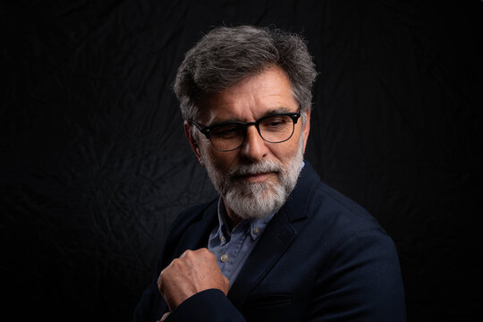Bearded mature businessman in serious low key portrait isolated on dark studio background with chiaroscuro effect