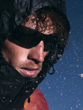 A male hiker in hiking clothes with a hood on his head and black sunglasses. Mountain hiking and a healthy lifestyle.